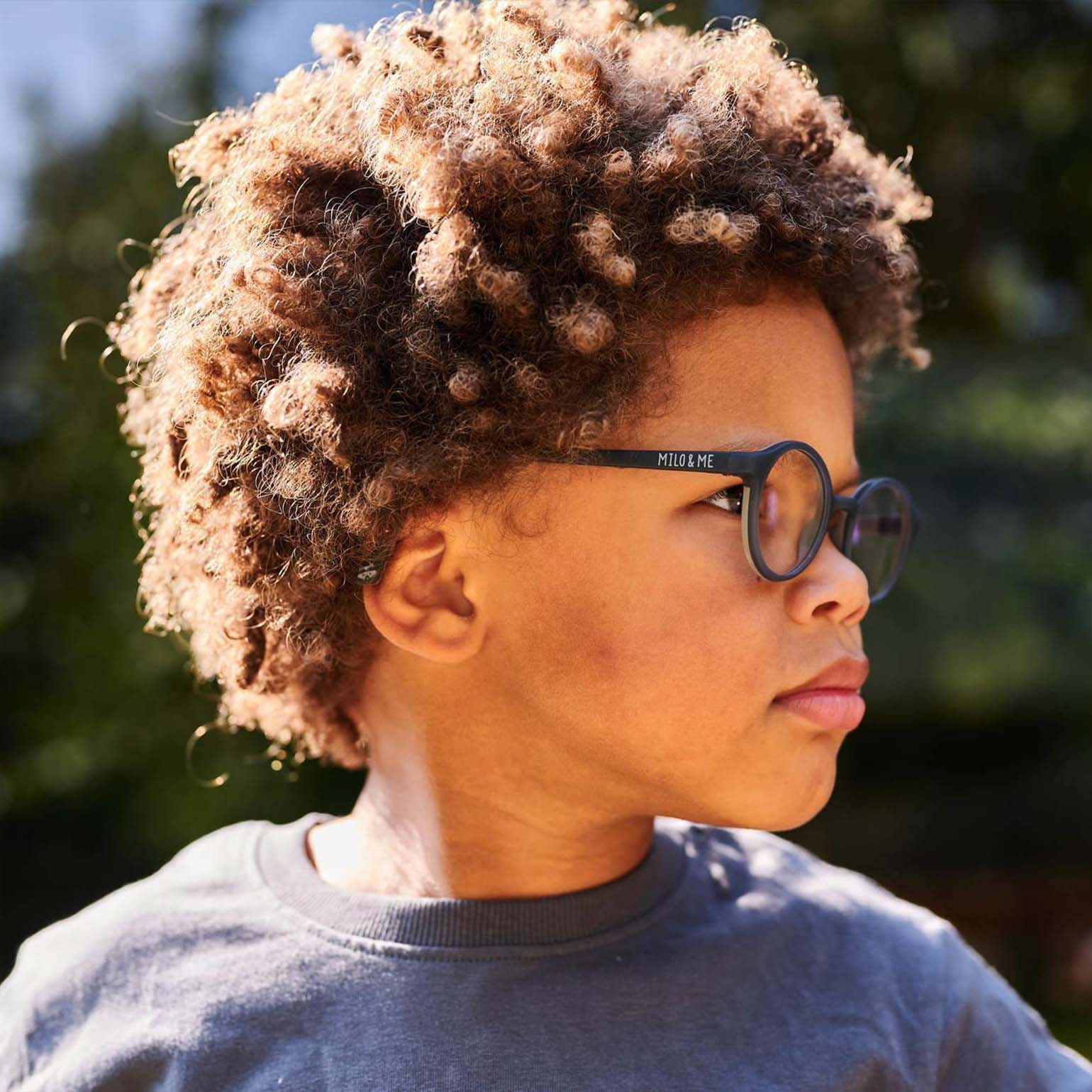 Milo & Me Kinderbrille Charly Grau Hellgrau Junge seitlich mit Rastalocken und dunkelblauem Oberteil 3 - 5 Jährige