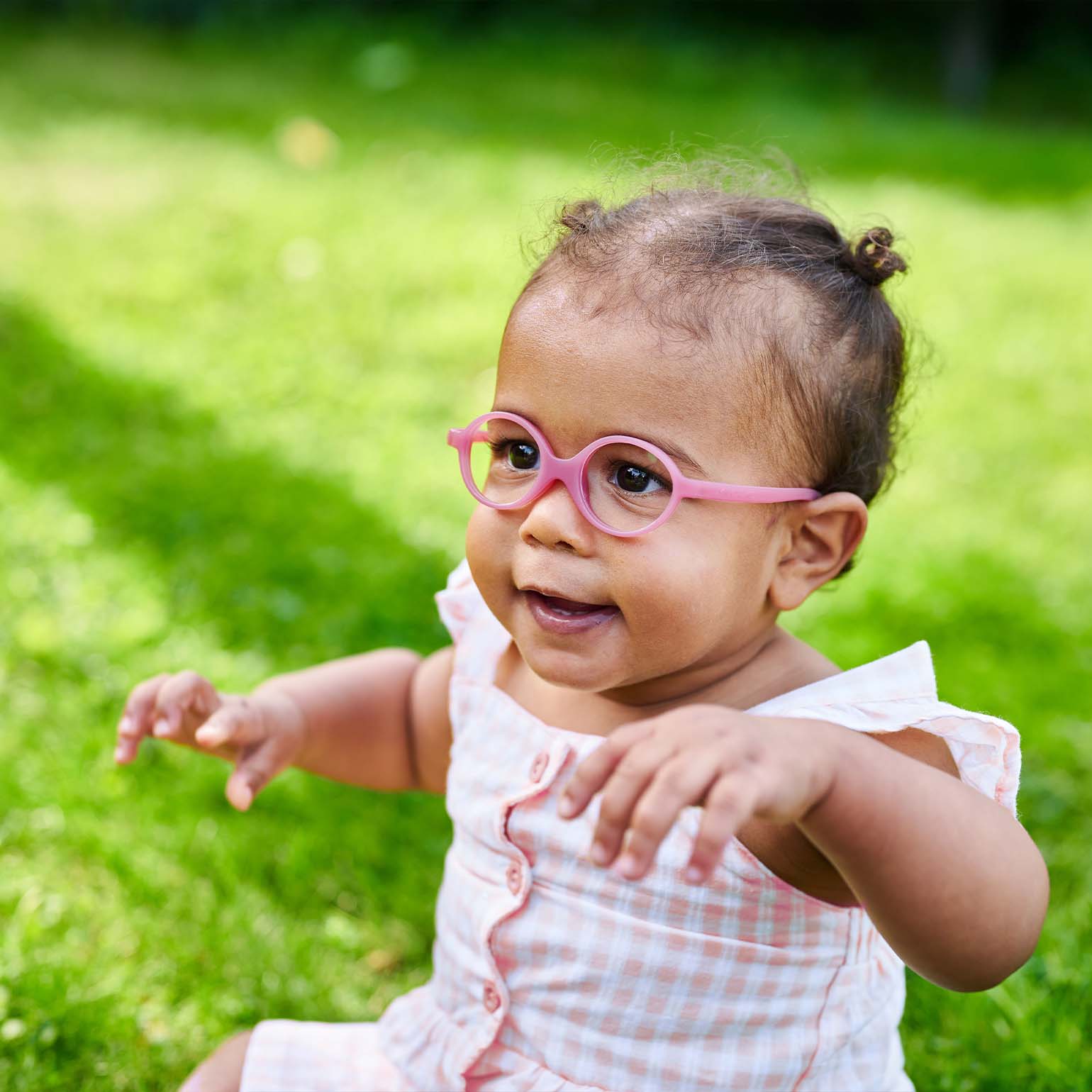 Milo & Me Babybrille Jessie Rosa Baby sitzend auf Wiese mit Rosa quadrierten Kleid 0 - 1 Jährige