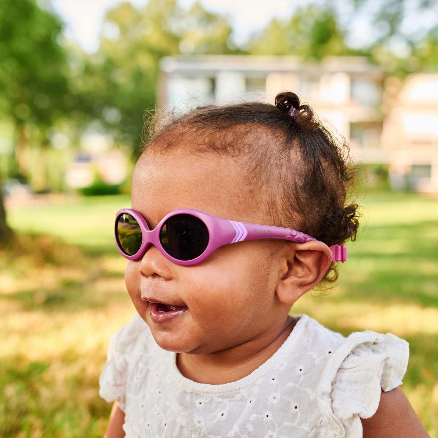 Milo & Me Kindersonnenbrille Nicky Brombeer Pink  Baby mit braunen Haaren und weißem Oberteil 12 - 24 Monate